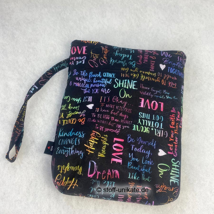 Gepolsterte Buchhüllentasche für Taschenbücher genäht aus reiner Baumwolle mit bunter Schrift auf Schwarz. Stoff-Unikate handmade in Germany